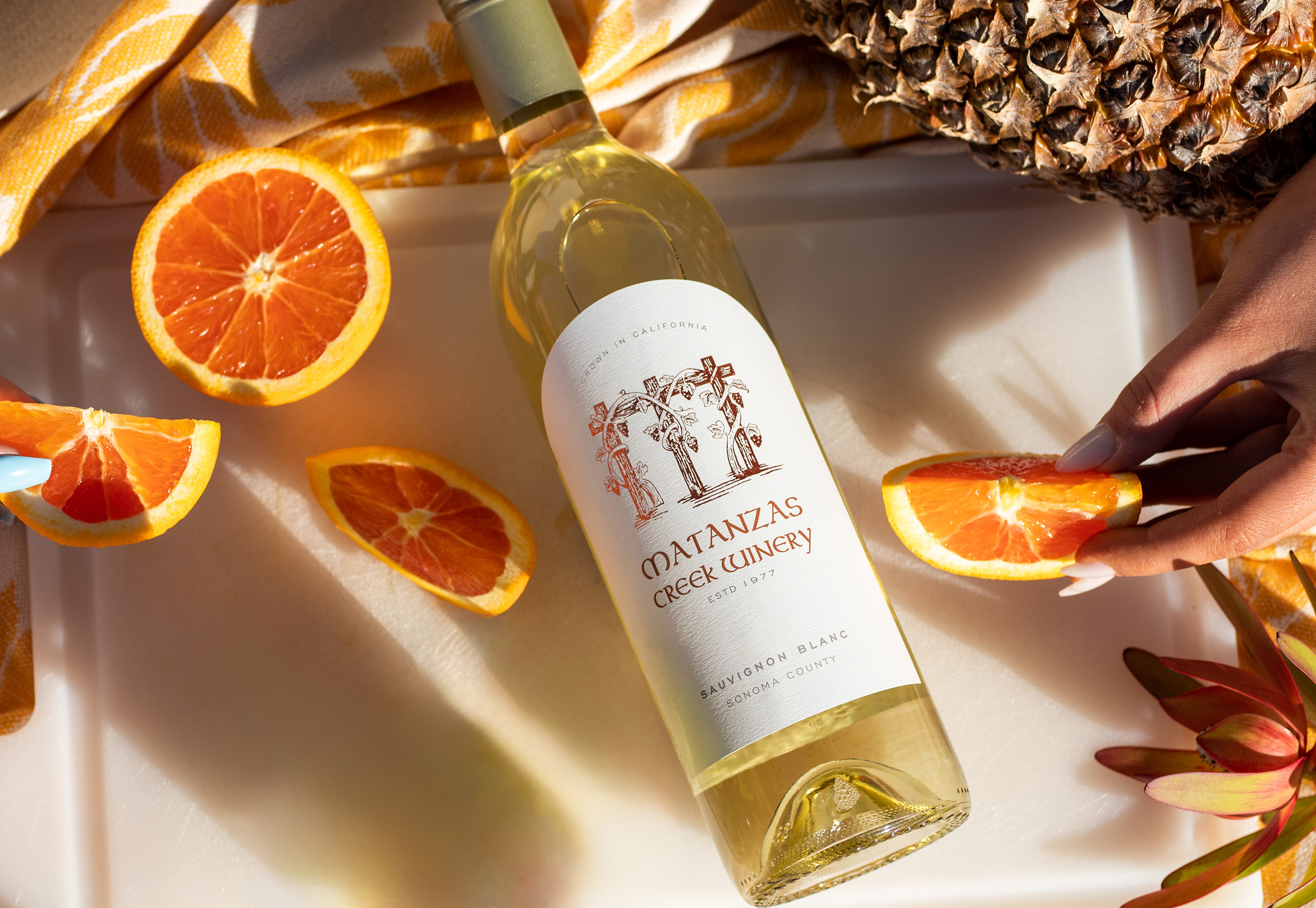 A bottle of white wine on a white cutting board with slices of orange around it, and a yellow blanket.
